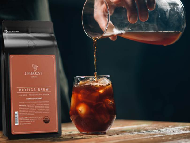 Bag of biotics cold brew coffee beans by Lifeboost on table whilst pouring fresh batch of coffee