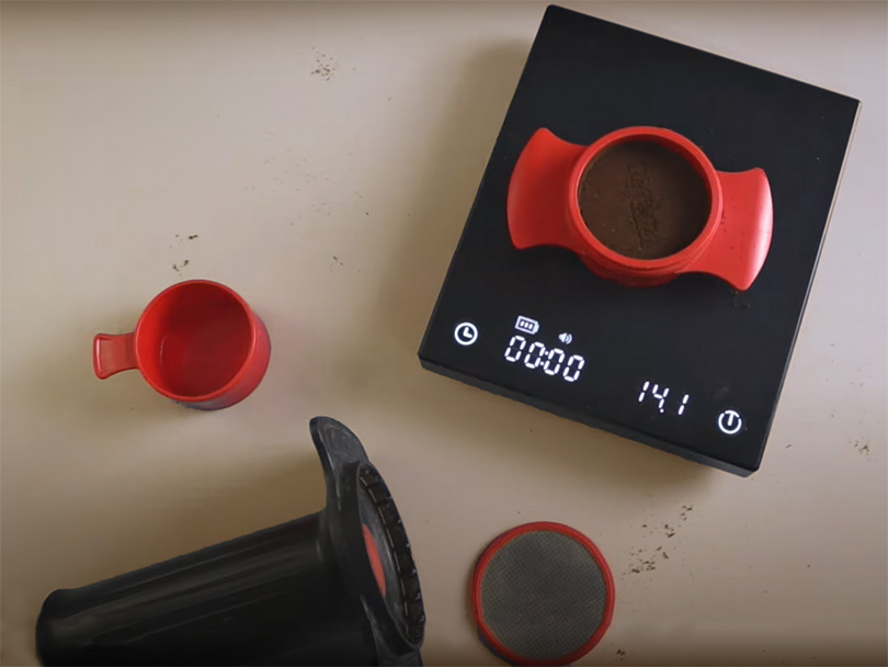 Parts of the Cafflano Kompresso laid out on counter with grounds basket on a coffee scale