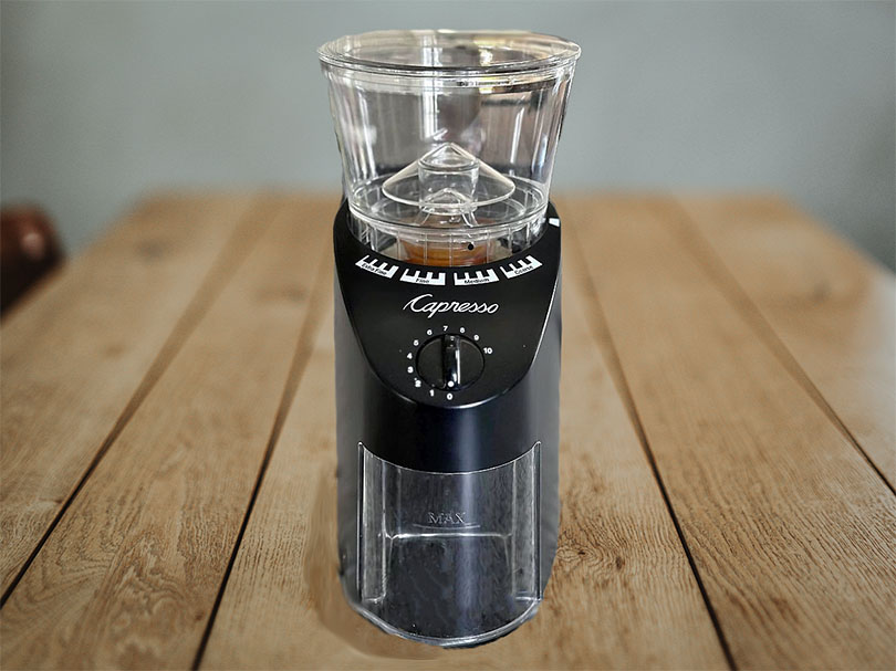 Front view of the Capreso Infinity electric burr grinder sitting on a wooden table
