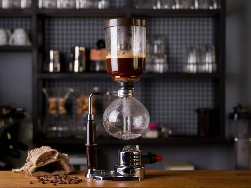 Hario Technica Siphon coffee maker on bench next to open bag of coffee beans