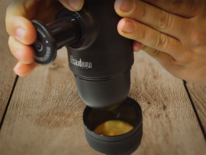 Hands pressing down on the manual pump of the Wacaco Minipresso to pull a fresh espresso shot into waiting cup