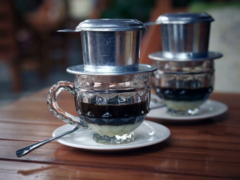 Phin (Vietnamese coffee maker) on top of a cup containing freshly made coffee with condensed milk