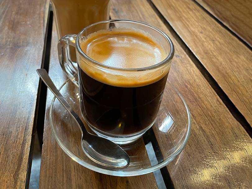 Lungo in a glass cup with saucer, sitting on a wooden table