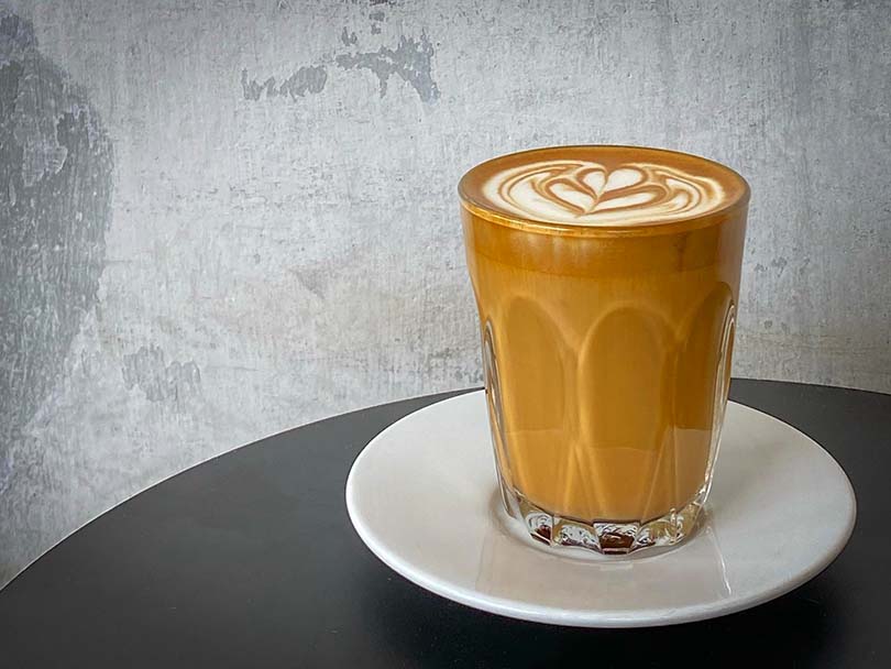 Breve coffee in a glass coffee cup, sitting on a dark table against grey wall