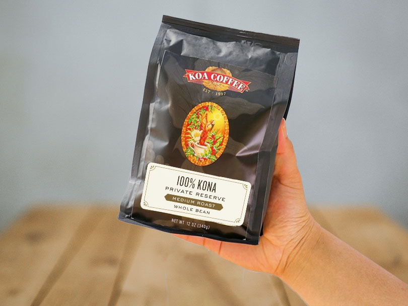 Hand holding bag of 100% Kona private reserve medium roast coffee beans (by Koa Coffee) towards the camera