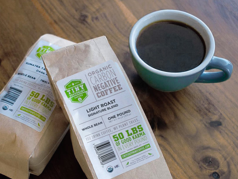 Tiny Footprint Light Roast Signature Blend on top of Sumatra coffee beans with cup of black coffee to the side