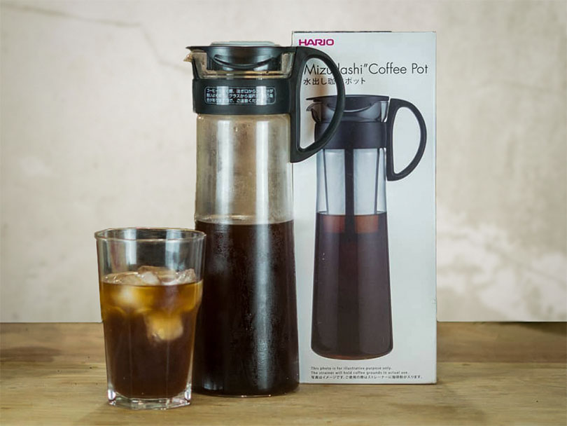 Half full Hario Mizudashi beside its box and a glass of cold brew coffee