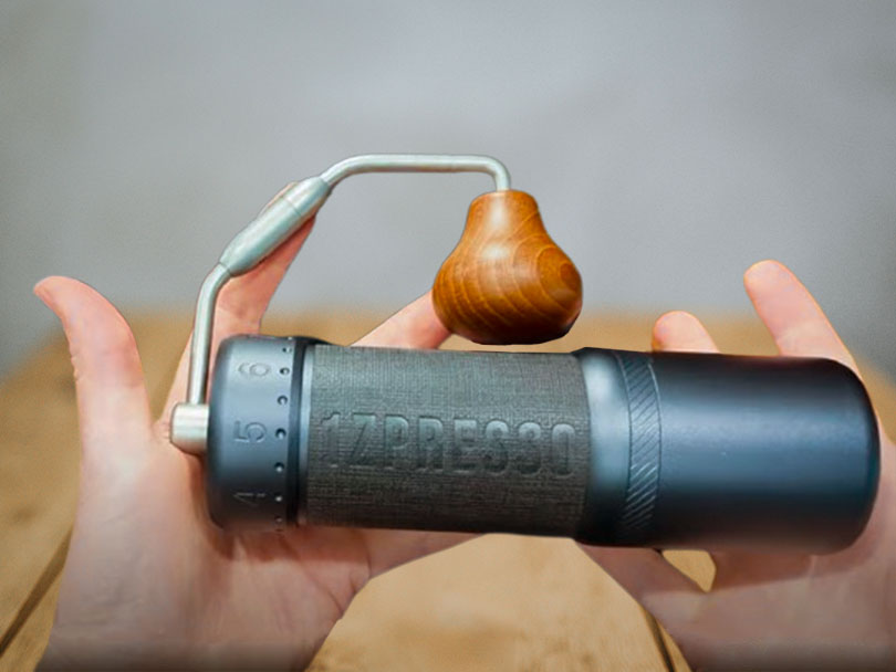 Two hands holding the 1Zpresso J Ultra flat, the foldable handle is attached