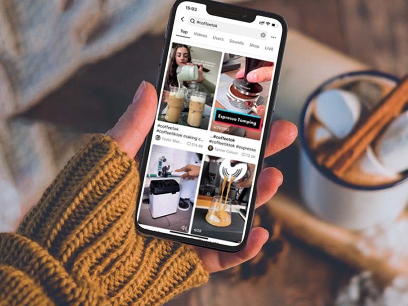 Woman's hand holding an iPhone with #coffeetok on the screen