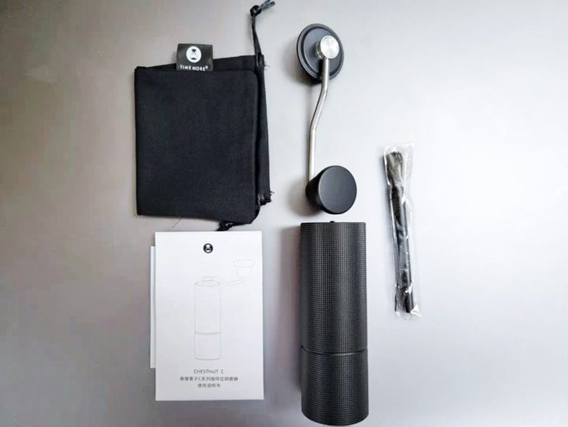 Flatlay of Timemore C3 grinder, its handle, cleaning brush, cloth bag, and instruction manual