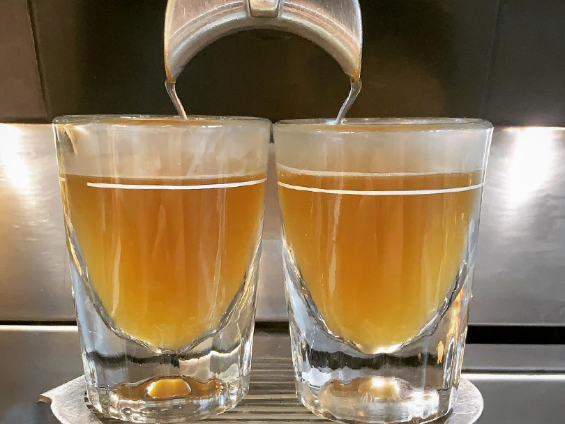 Two freshly made espresso shots with pale white coffee beans