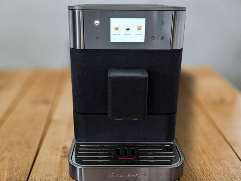 Front view of the KitchenAid KF7 espresso machine, turned on, sitting on a wooden table