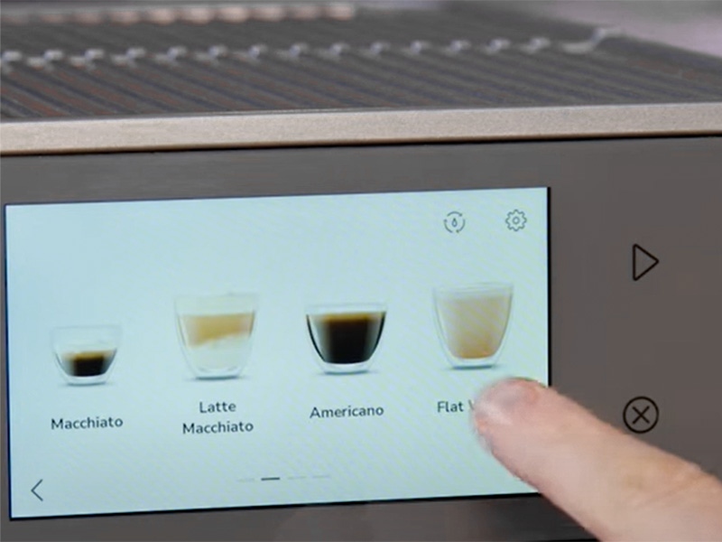 A finger scrolling through the coffee drinks options on the KitchenAid KF8's touchscreen