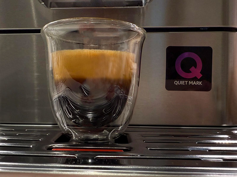 Close up of the Quiet Mark certification on a KitchenAid super automatic espresso machine, with a freshly made shot of espresso on the drip tray