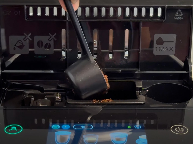 Using the built-in coffee scoop to pour pre-ground coffee into the chute of the Rivelia espresso machine