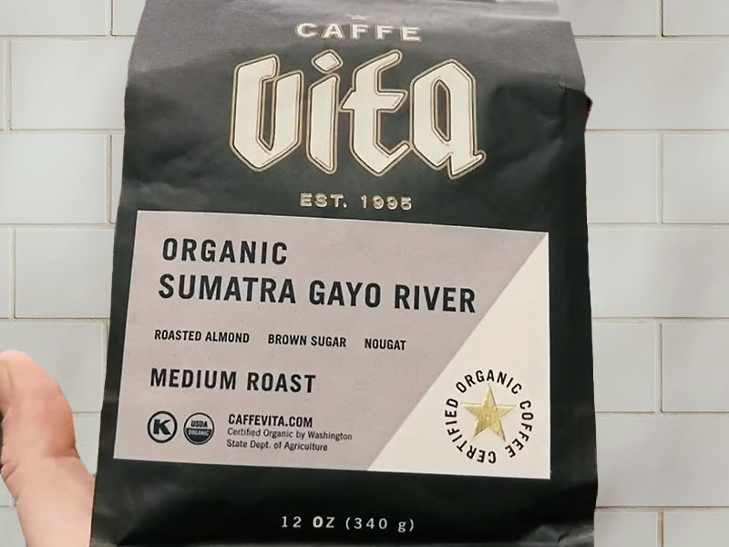Caffe Vita - Organic Sumatra Gayo River (Medium Roast) held against white kitchen tiles