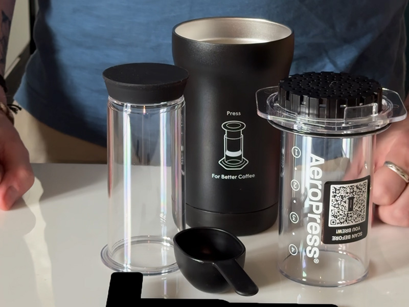AeroPress Go Plus parts on counter (coffee maker/plunger, coffee scoop, stirrer, thermos cup)