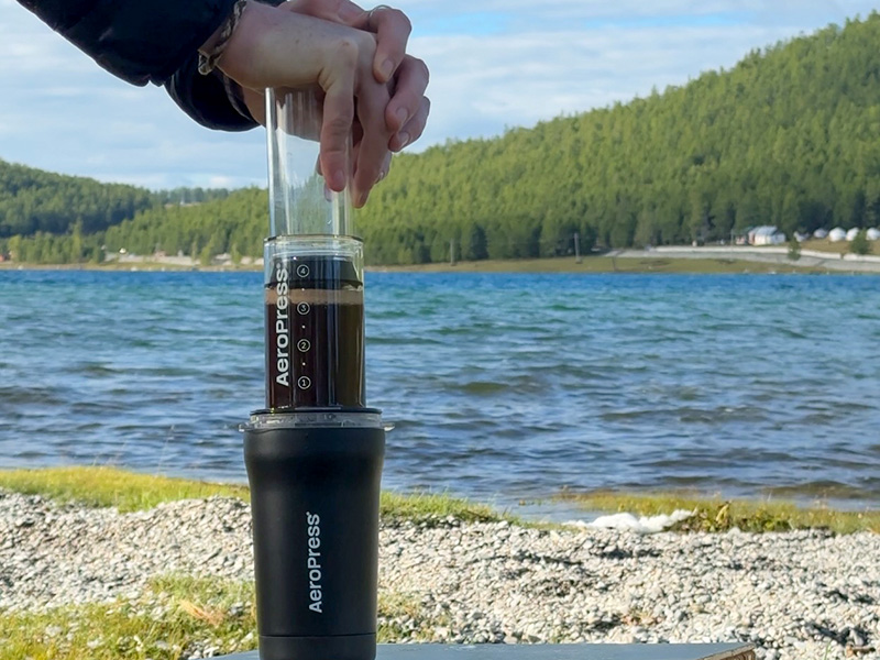 Hands pressing down on the AeroPress coffee brewer using the inverted method with Lake Khuvsgul in the background