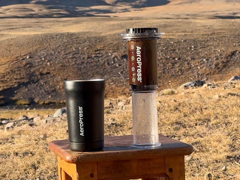 AeroPress Go Plus brewing coffee using the inverted method, with the insualted travel mug to its left