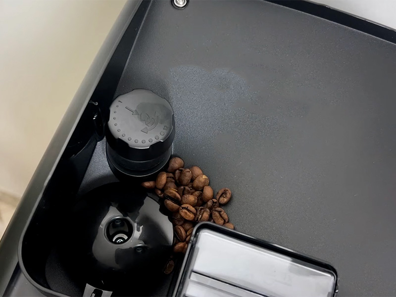 Top-down view of the bean hopper with a small number of coffee beans, and the ceramic burr grinder adjustment dial of the Philips 4400