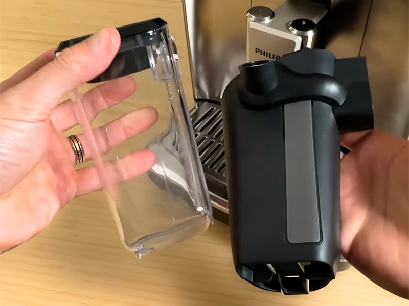 Hands holding the Philips 4400 LatteGo milk container parts in front of the machine