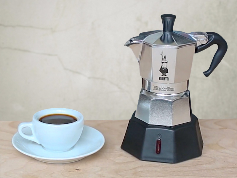 Bialetti Moka Elettrika (electric moka pot) sitting on table beside freshly made cup of coffee