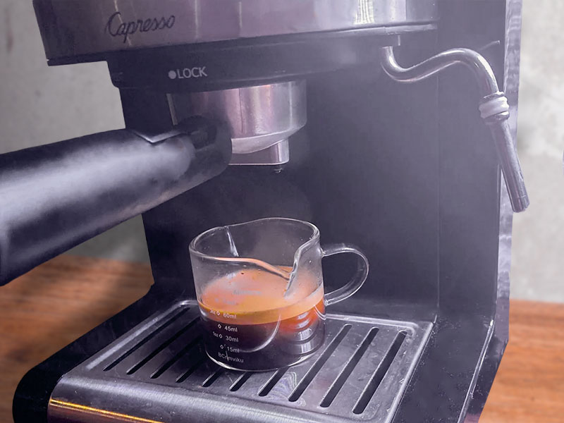 A shot of freshly made espresso with crema sitting in a transparent cup on the drip tray of the Capresso EC100