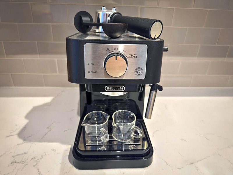 Front view of the DeLonghi Stilosa with glass espresso cups on drip tray and accessories sitting on top