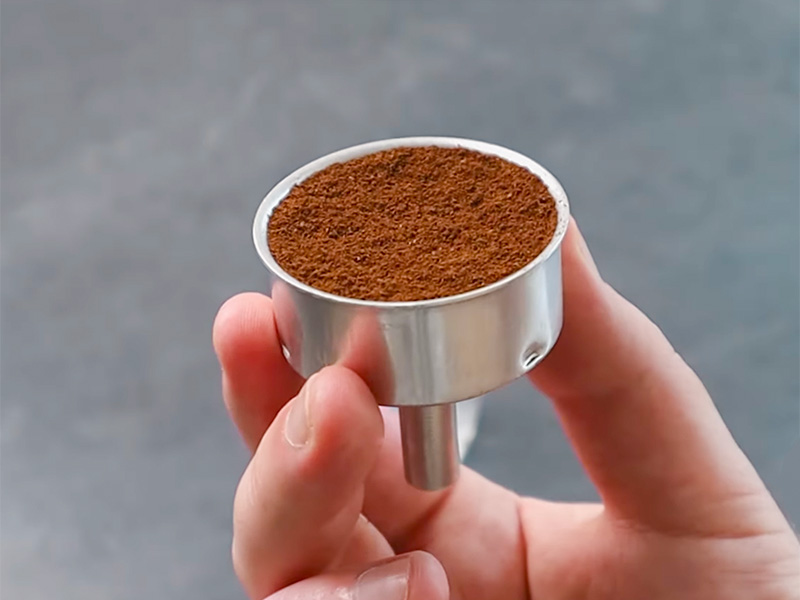 Holding a moka pot's filter basket in 1 hand to show the medium-fine ground coffee inside