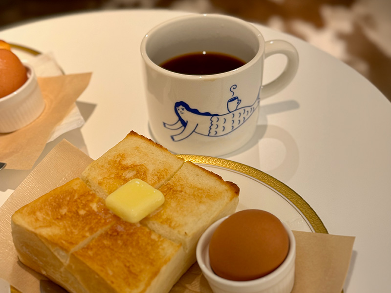 A mug of red-eye coffee, toast with butter, and a boiled egg on a white table