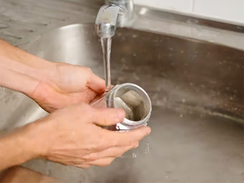Hands holding the bottom chamber of the Bialetti Moka Express under the faucet to clean it