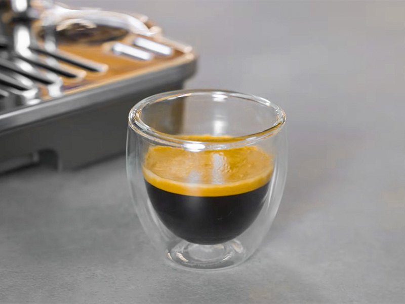 Shot of espresso with thick crema in a glass, sitting in front of DeLonghi La Specialista Touch