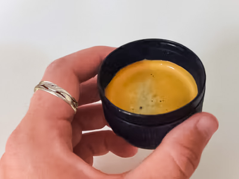 Hand holding the Wacaco Minipresso cup with freshly made espresso with crema