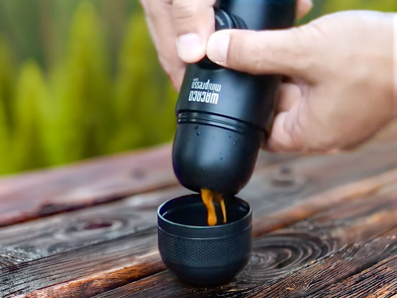 Hands manually pumping the Wacaco Minipresso, with an espresso shot coming out into the waiting cup