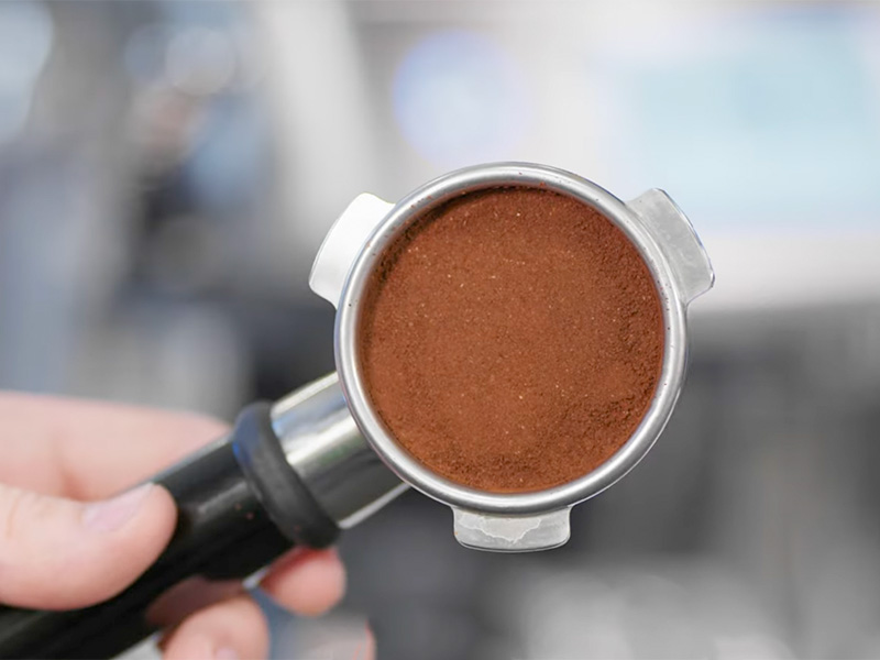 Hand holding up the portafilter for the Breville Barista Touch Impress following the auto dosing and tamping