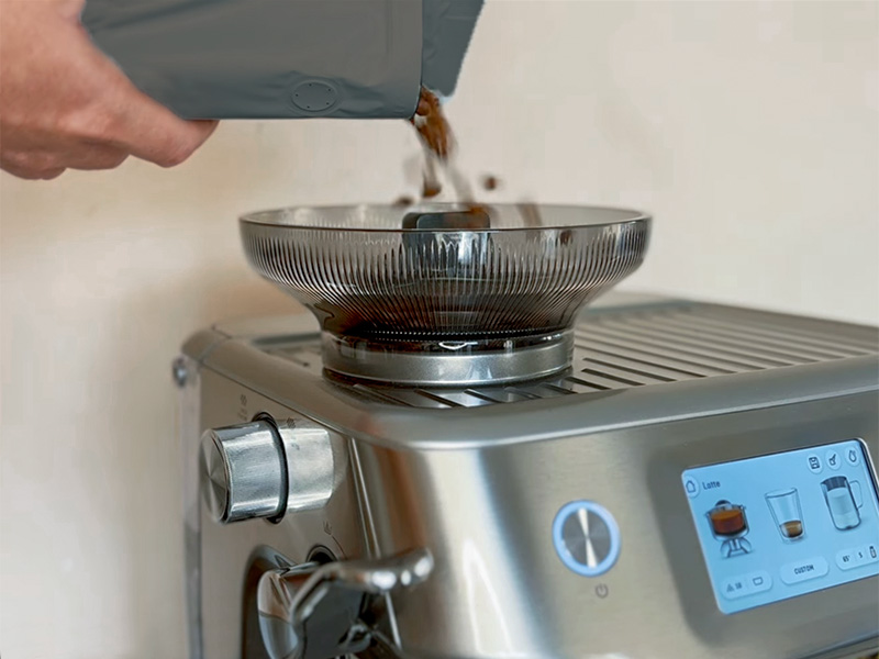 Pouring coffee beans into the bean hopper of the Breville Barista Touch Impress