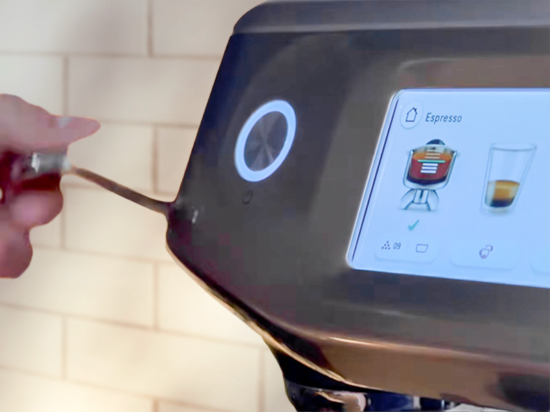 Hand pulling down the tamp handle of the Breville Barista Touch Impress espresso machine, the on-screen indicator has a green tick