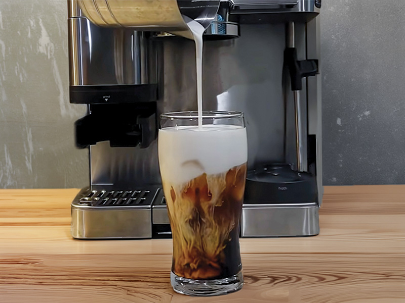 Pouring cold foam into cold brewed coffee, in front of the Ninja Luxe Cafe Pro machine