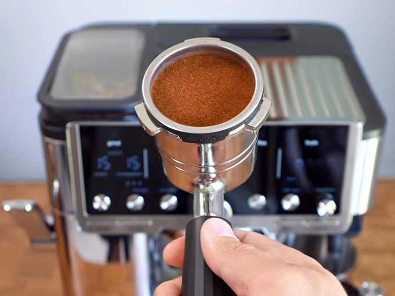 Hand holding the portafilter in front of the Ninja Luxe Cafe Pro, with freshly dosed and tamped ground coffee