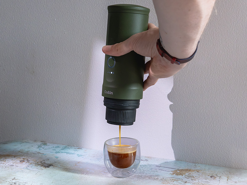 Hand holding the Outin Nano above a glass whilst it pulls a shot of espresso