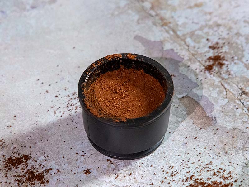 Lightly tamped ground coffee in the standard basket of the Outin Nano - coffee grounds scattered on table as it's messy to use
