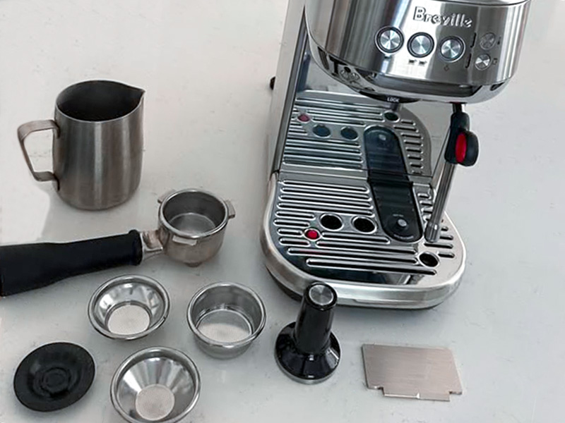 All the parts for the Breville Bambino Plus laid out on table in front of the espresso machine