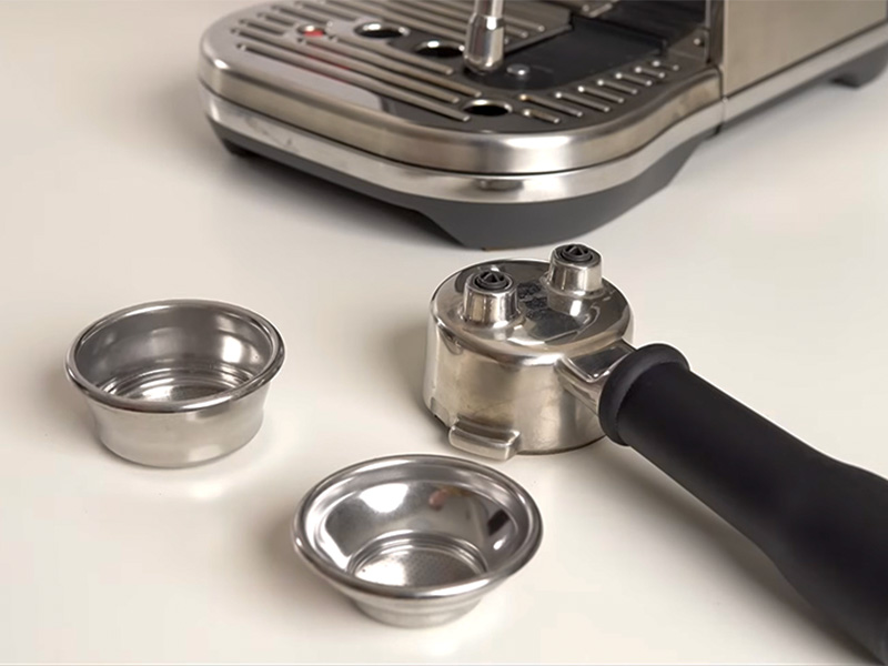 Close-up of the 54mm portafilter and both the single and dual-walled baskets that come with the Breville Bambino Plus (pictured in the background)