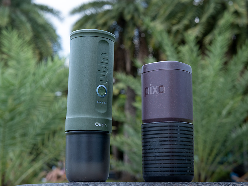 The taller, narrower OutIn Nano facing towards the shorter Wacaco Pixapresso, with trees in the background