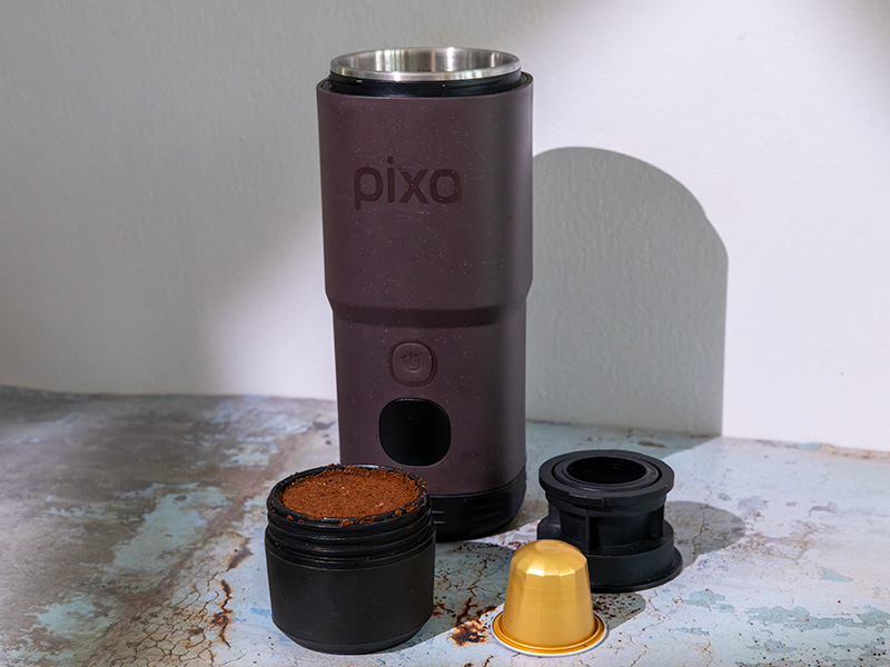 Wacaco Pixapresso on table with full ground coffee basket, Nespresso pod, and Nespresso basket