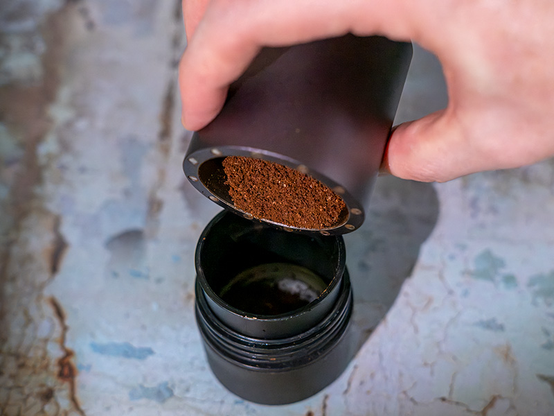 Pouring freshly ground coffee into the Wacaco Pixapresso's grounds basket, with the help of the included dosing funnel