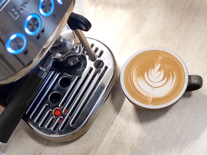 A freshly made latte with simple latte art, sitting on the table in front of the Breville Bambino Plus