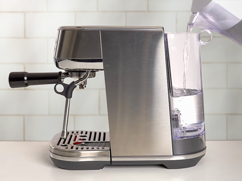 Pouring water into the Breville Bambino Plus' water tank using a jug