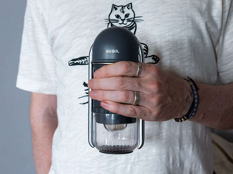 Man's hand holding the HUGH Leverpresso Lite V4 against a white cat t-shirt