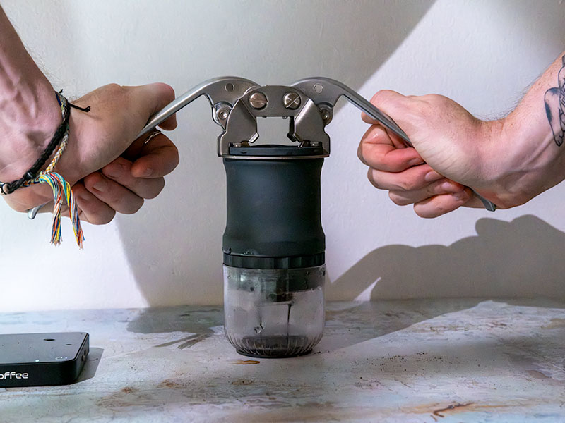 Two hands pulling down the lever arms of the Leverpresso Lite V4, shot starting to pull into the attached cup. A coffee scale is set off to the side